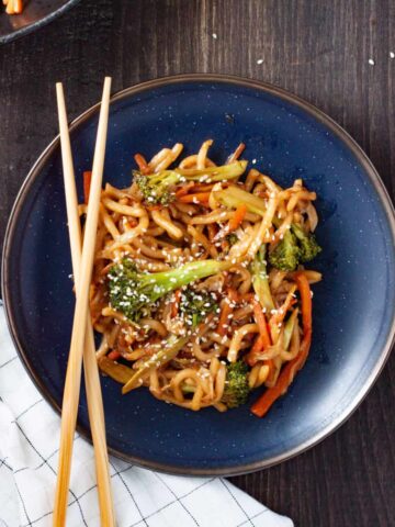 A plate with teriyaki udon and vegetables with chopsticks on the side of the plate.