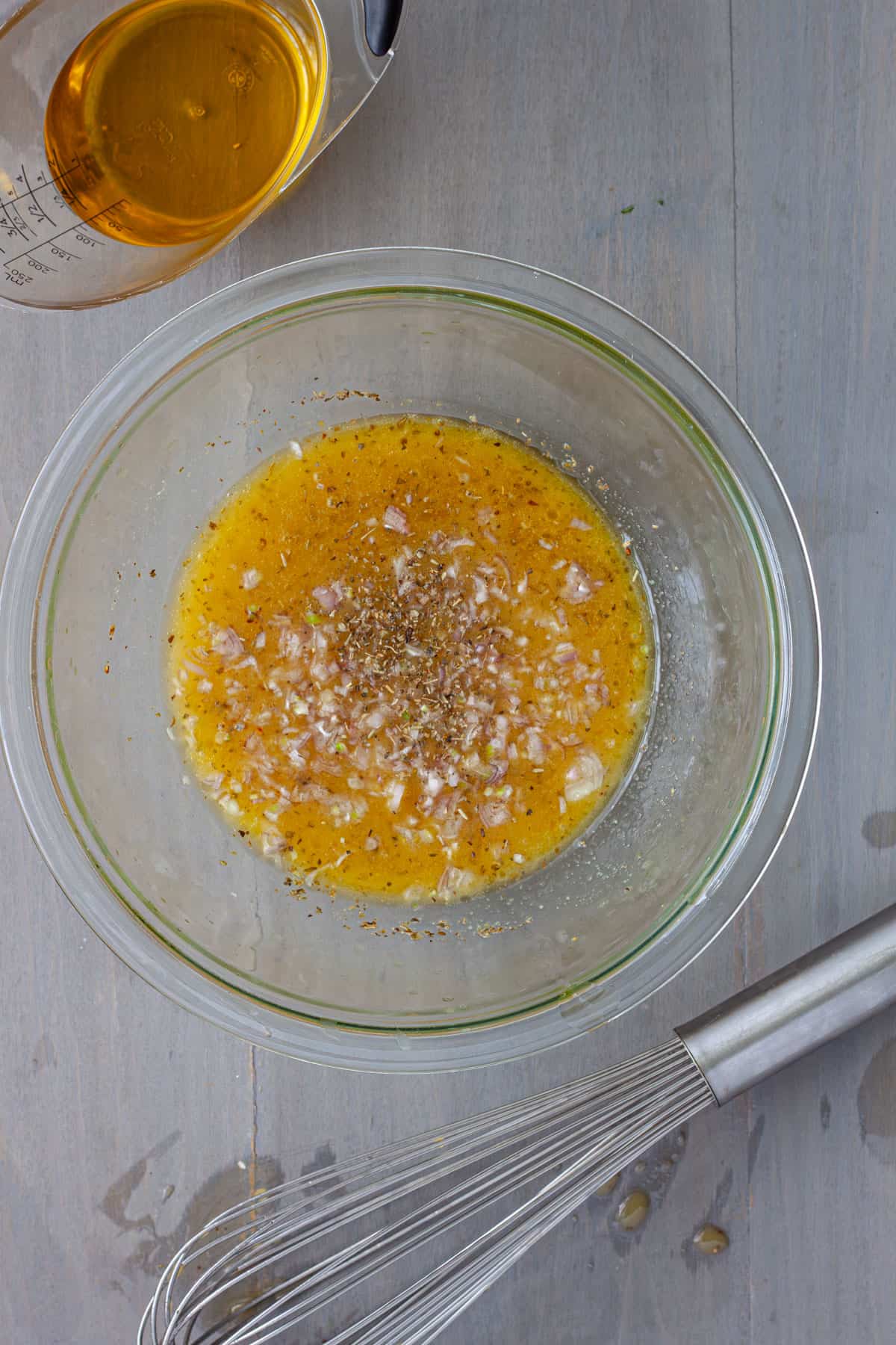 Shallots added to a white balsamic vinaigrette in a medium bowl.