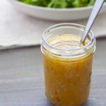 White balsamic vinaigrette in a mason jar with a spoon and bowl of greens in the background.