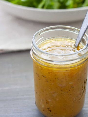 White balsamic vinaigrette in a mason jar with a spoon and bowl of greens in the background.