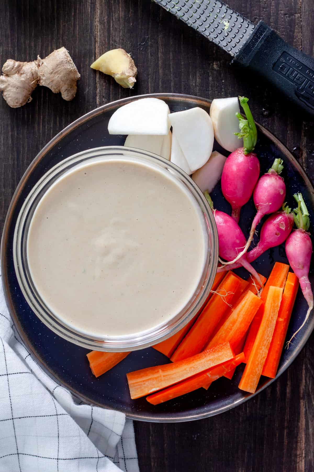 Miso and tahini dressing in a small bowl on a plate with a colorful assortment of vegetables.