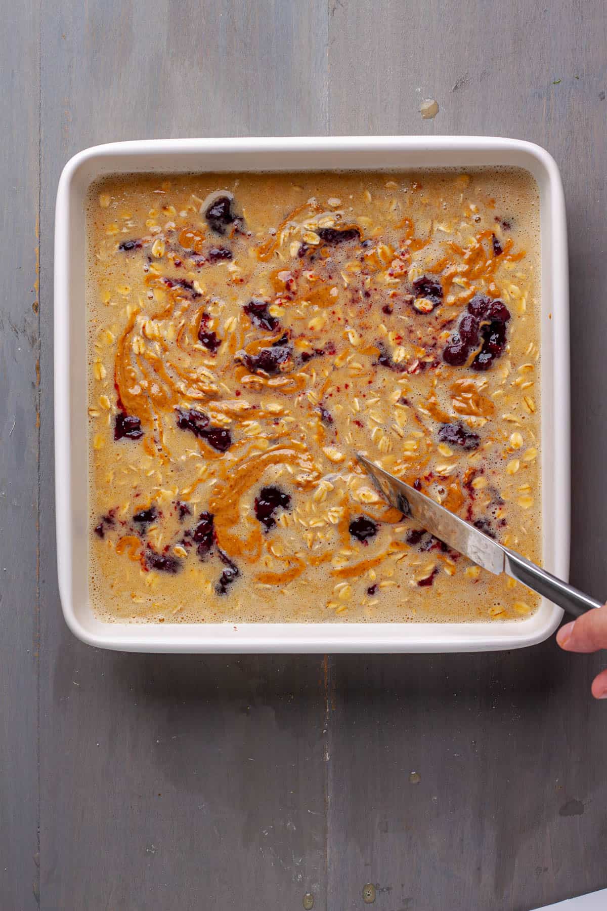 A knife swirling peanut butter and jam throughout a baked oatmeal.