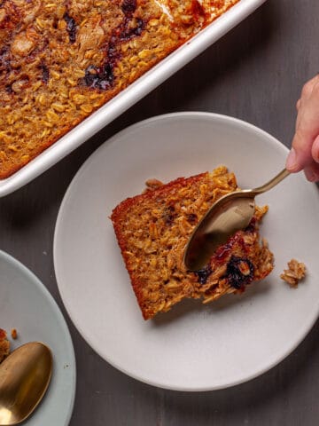 A portion of peanut butter and jam baked oatmeal with a spoon cutting into the portion.
