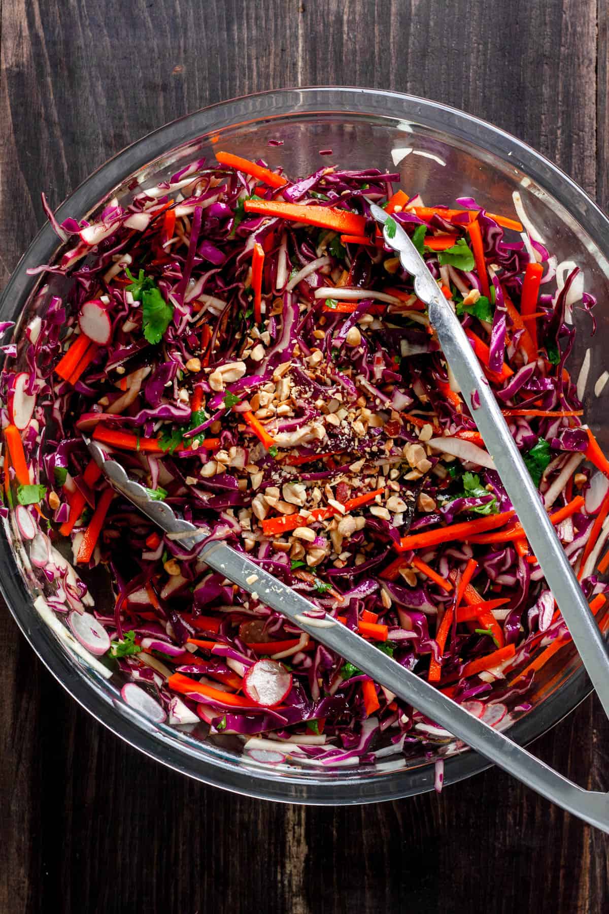 A purple cabbage slaw in a large mixing bowl tossed well with chopped peanuts on top.