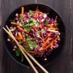 Purple cabbage slaw in a large black serving bowl with chopsticks to the side.