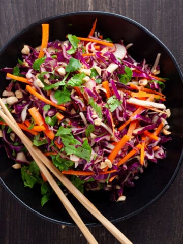 Purple cabbage slaw in a large black serving bowl with chopsticks to the side.