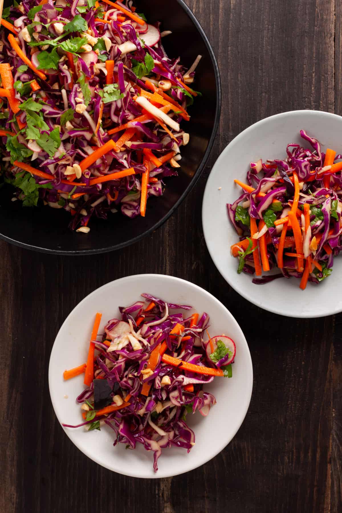 Purple cabbage slaw in a large serving bowl with two portions on small plates.
