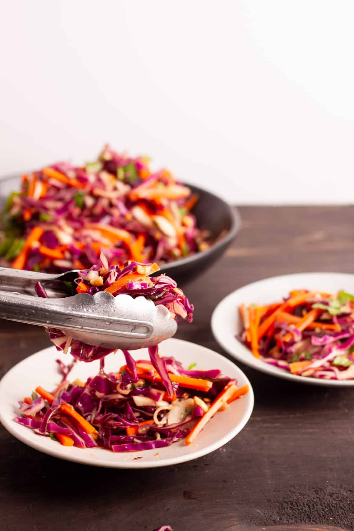 A serving of purple cabbage slaw getting placed on a small white plate.