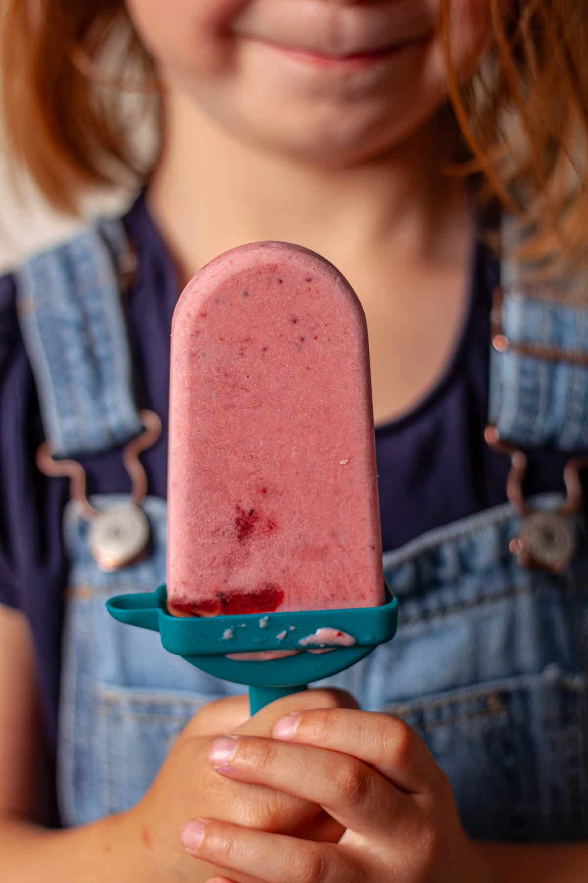 A young girl holding a roasted strawberries and cream popsicle.