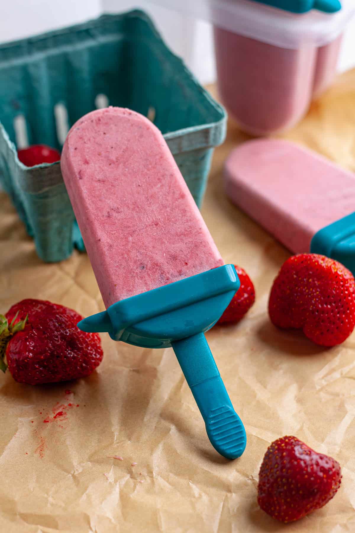Roasted strawberries and cream popsicles on a table with fresh strawberries.