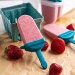 Roasted strawberries and cream popsicles on a table with fresh strawberries.