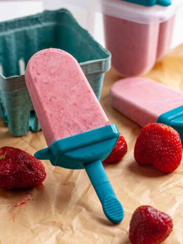Roasted strawberries and cream popsicles on a table with fresh strawberries.