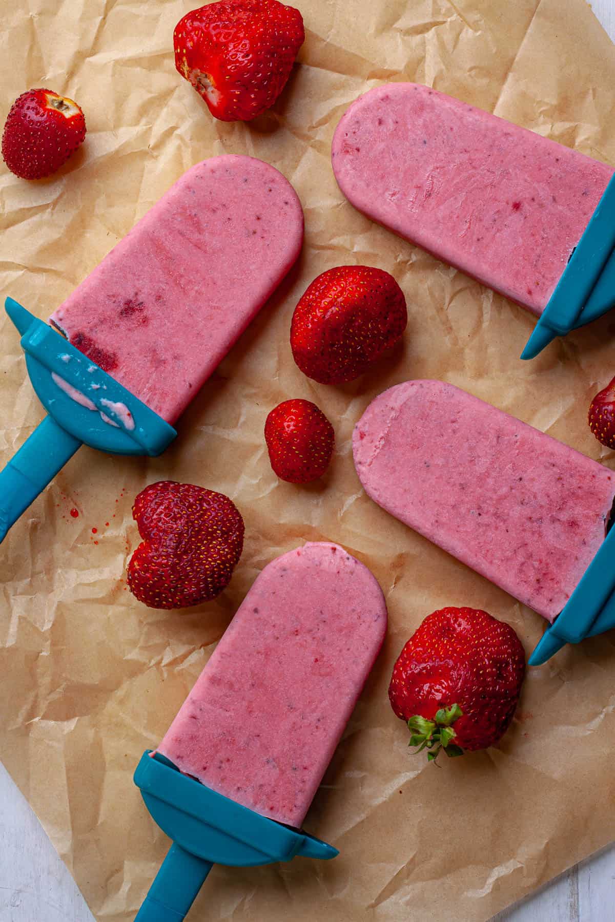 Roasted strawberry and cream popsicles on a platter with whole fresh strawberries.