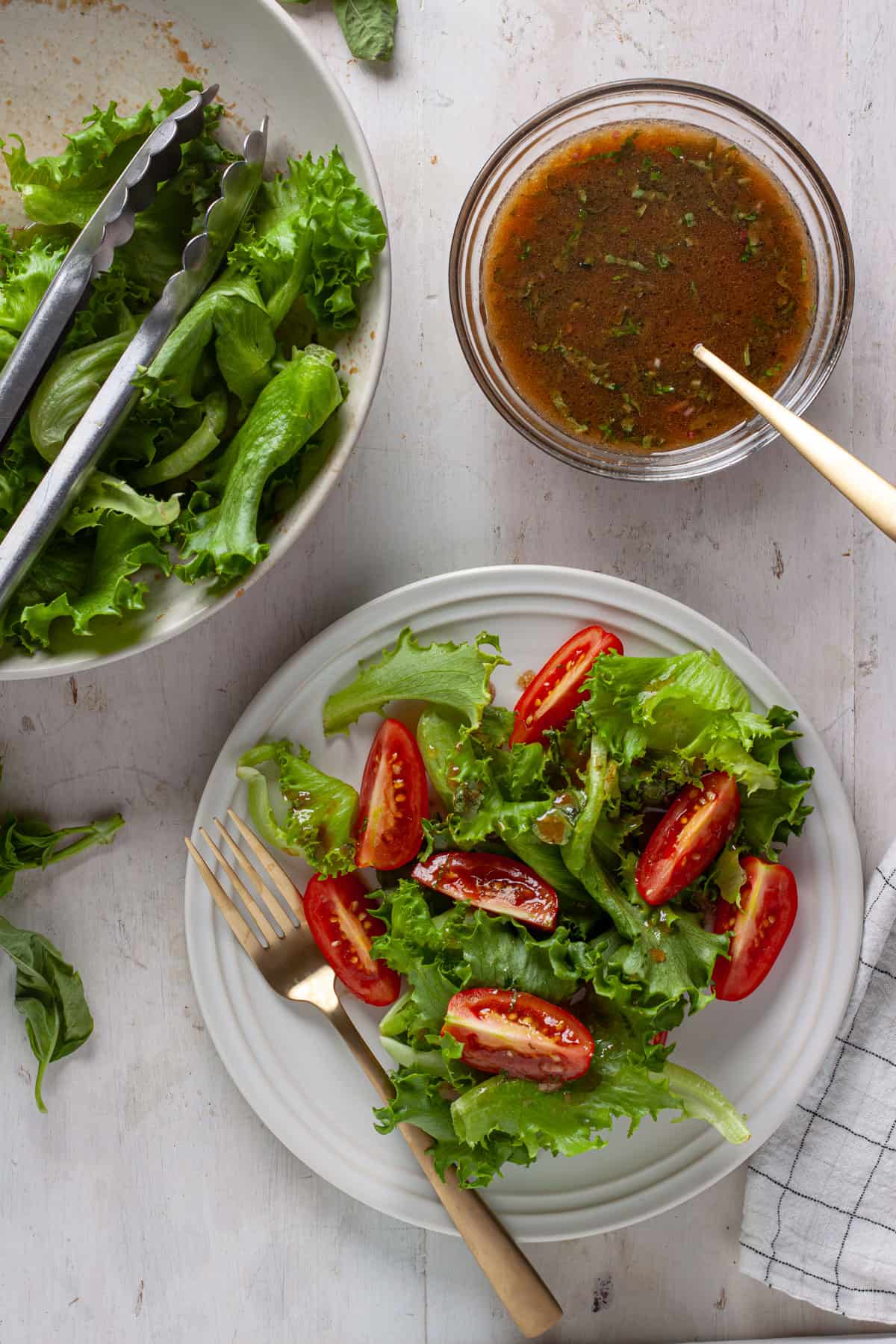A simple side salad with greens and tomatoes with basil balsamic vinaigrette to the side.