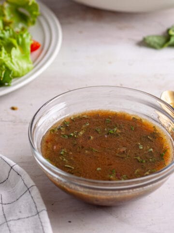 A small bowl of basil balsamic vinaigrette with a salad in the background.
