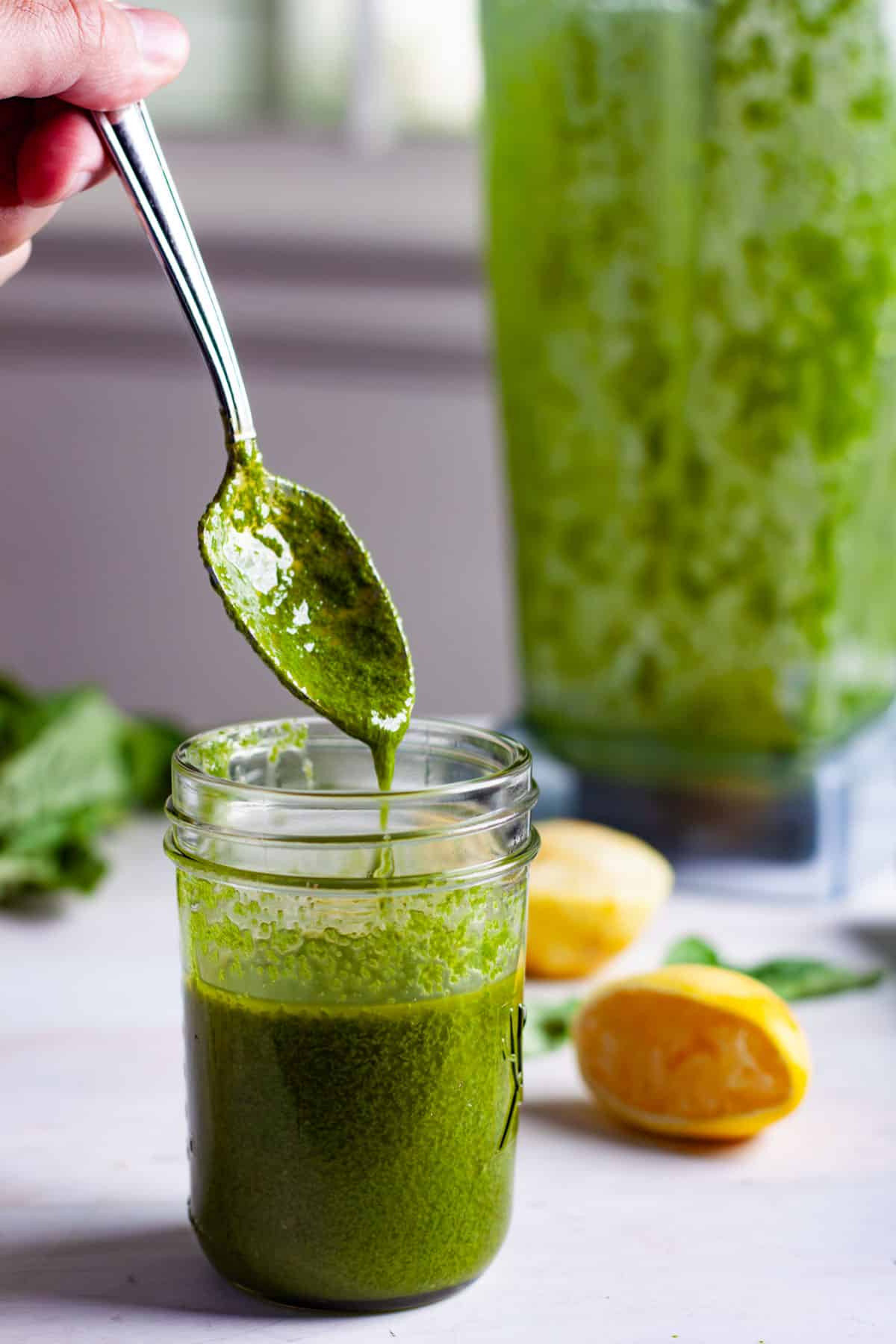 Basil vinaigrette in a glass jar with a spoon dripping some of it into the jar.