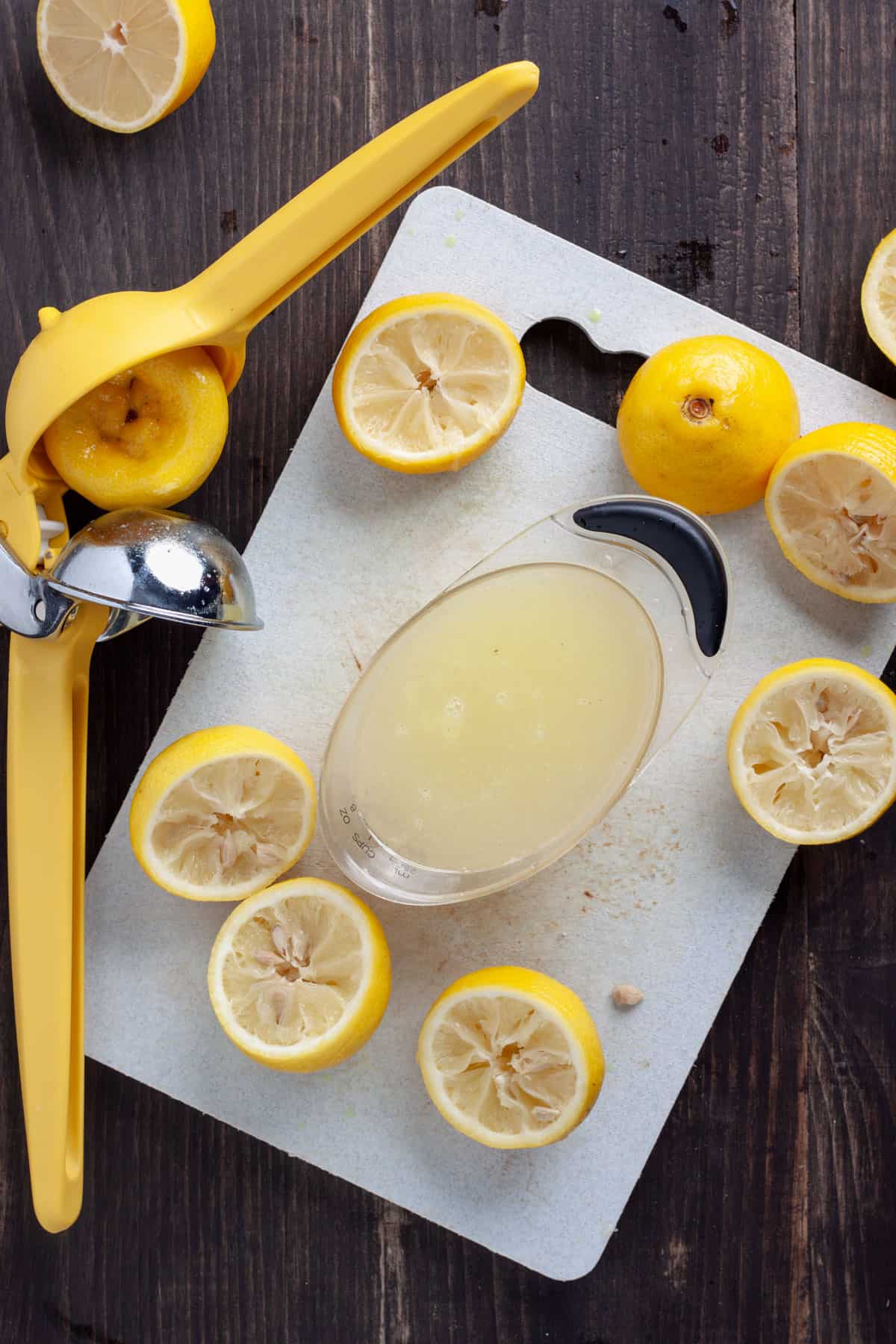 Lemons halved on a cutting board and juice squeezed into a measuring cup.