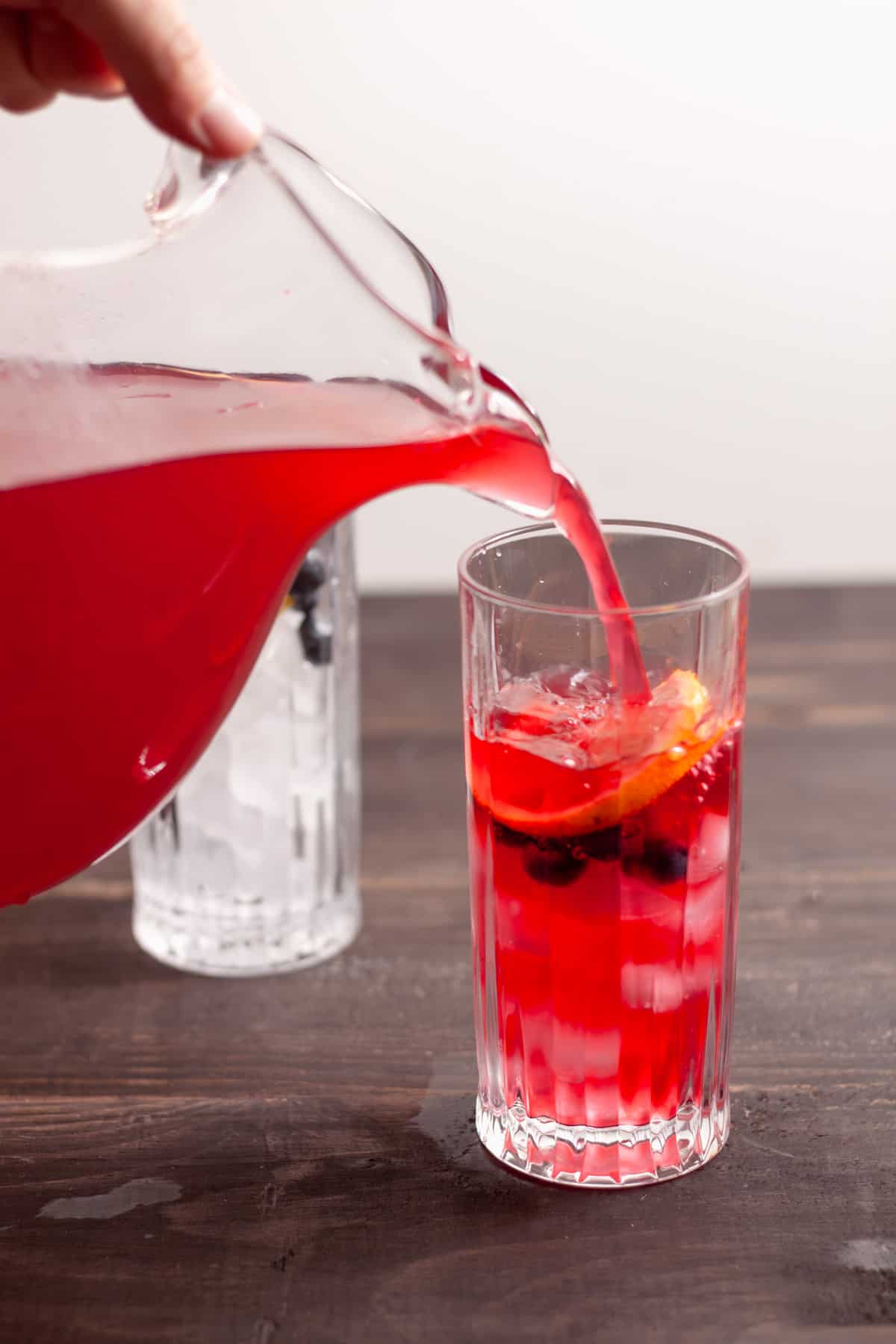 Blueberry lemonade pouring into a glass with ice, blueberries and lemon.
