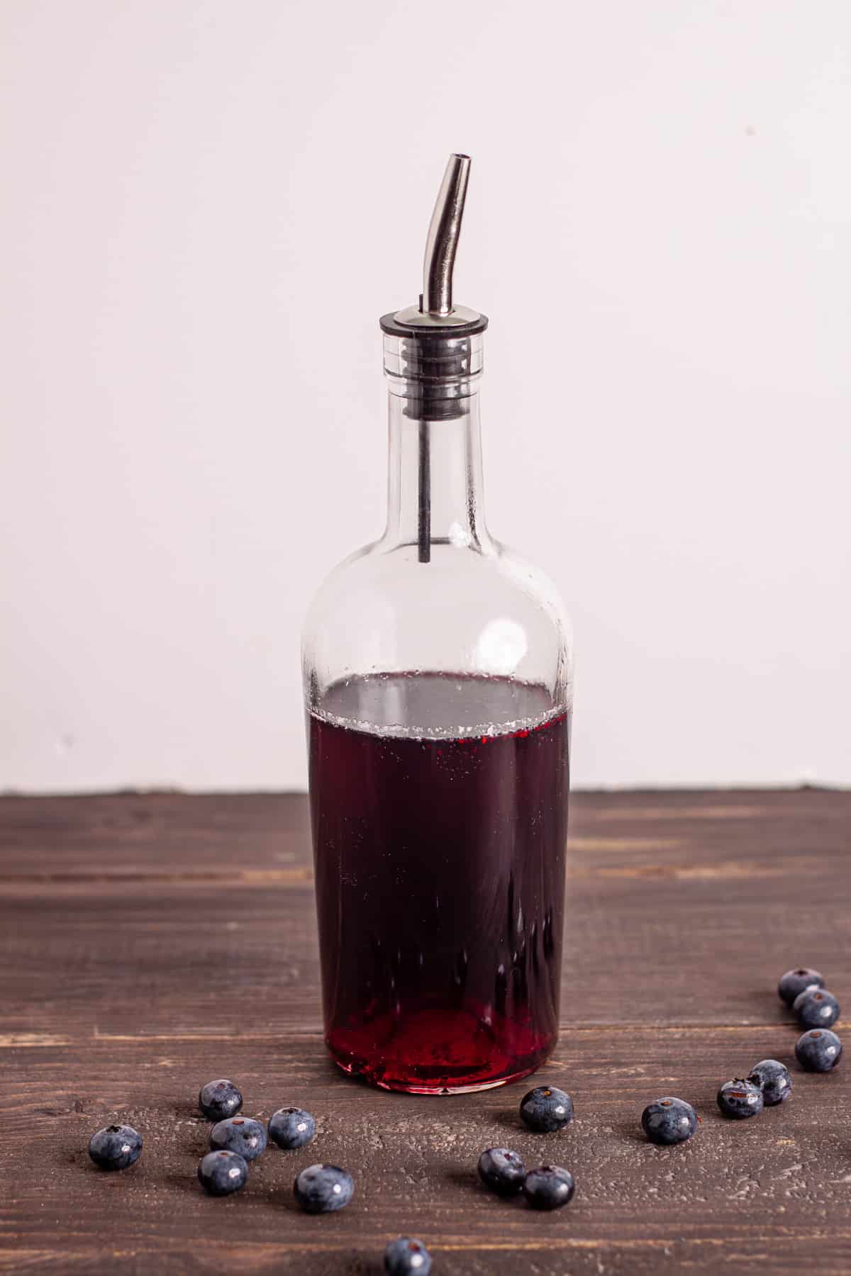 A glass bottle with blueberry simple syrup and blueberries on a dark table.