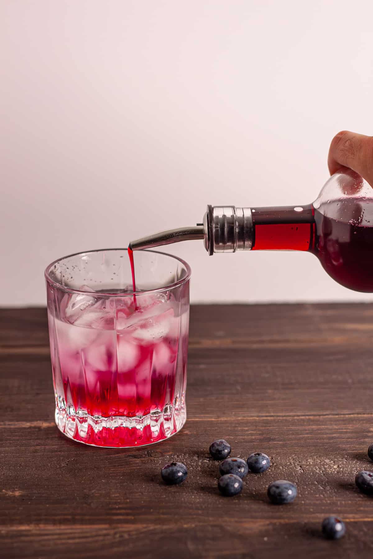 Blueberry simple syrup pouring into a glass with ice and water.