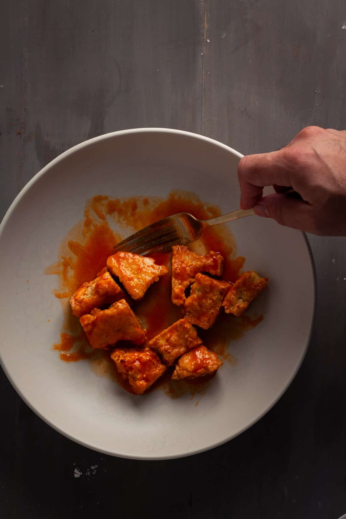 Crispy buffalo tofu getting tossed in a bowl.