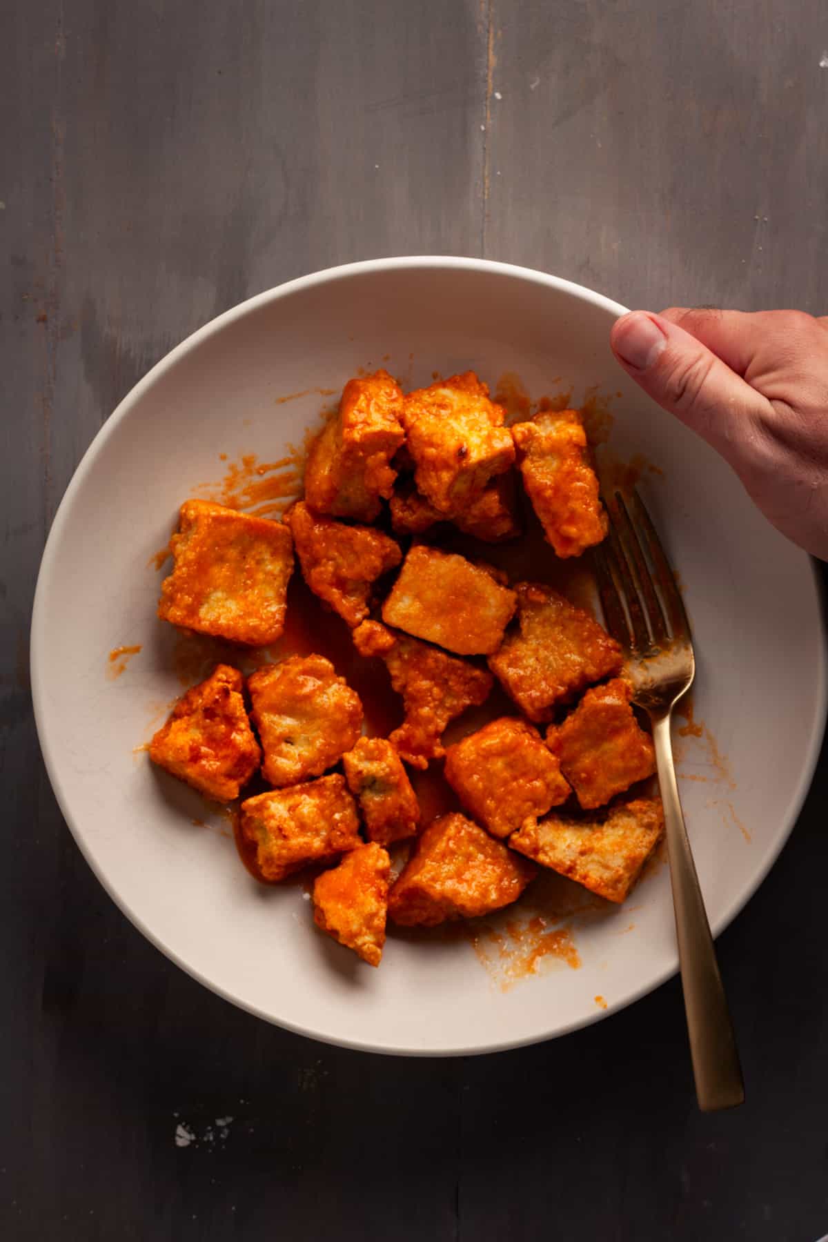 A bowl of crispy buffalo tofu getting picked up.
