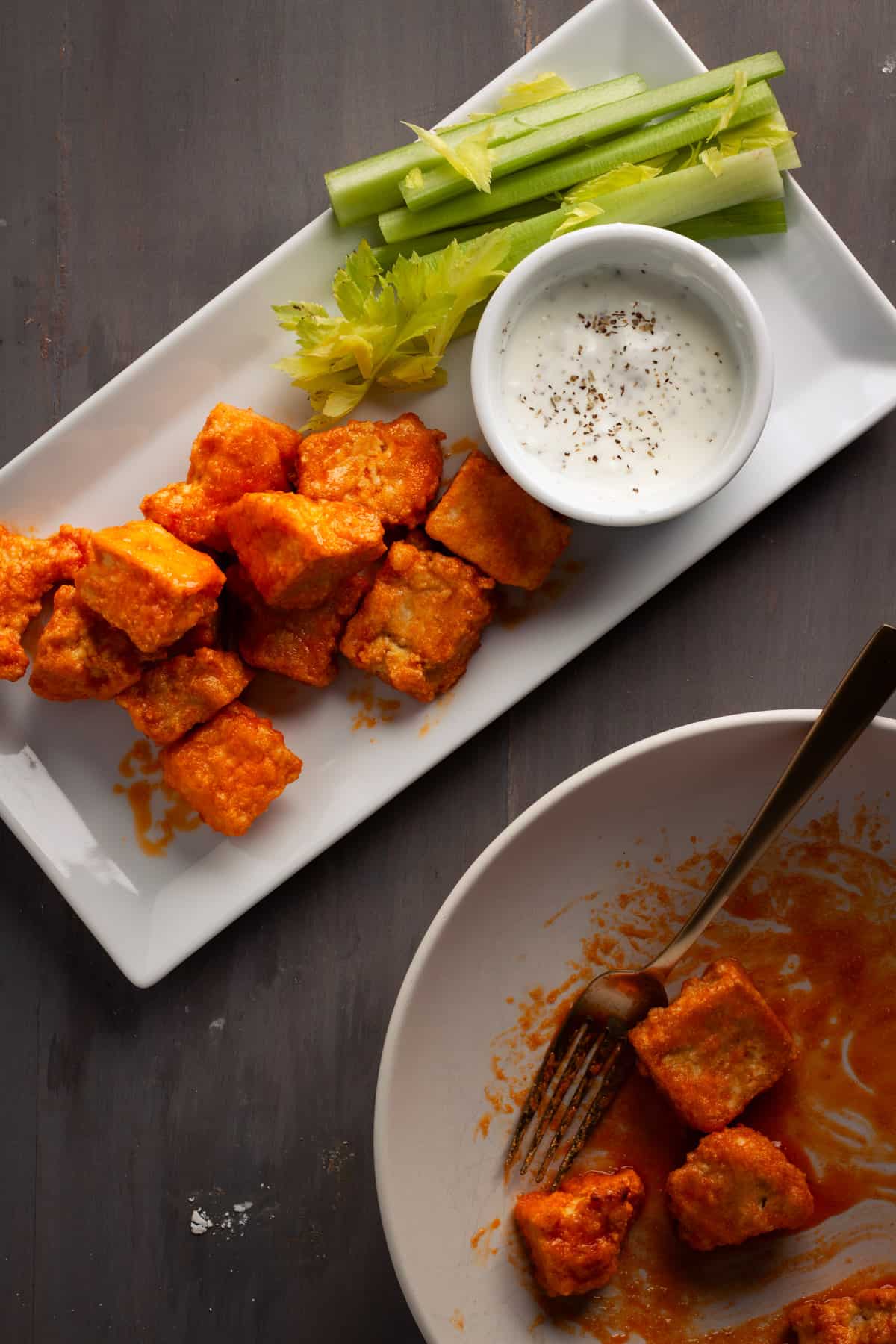 Crispy buffalo tofu on a serving platter with sticks of celery and a dipping sauce.