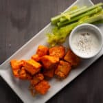 Crispy buffalo tofu nuggets on a platter with a dipping sauce and celery.