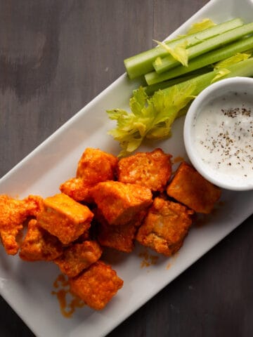 Crispy buffalo tofu nuggets on a platter with a dipping sauce and celery.