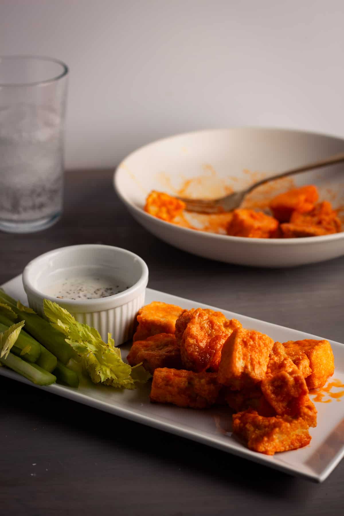 Crispy buffalo tofu on a serving platter with celery sticks and a dipping sauce.