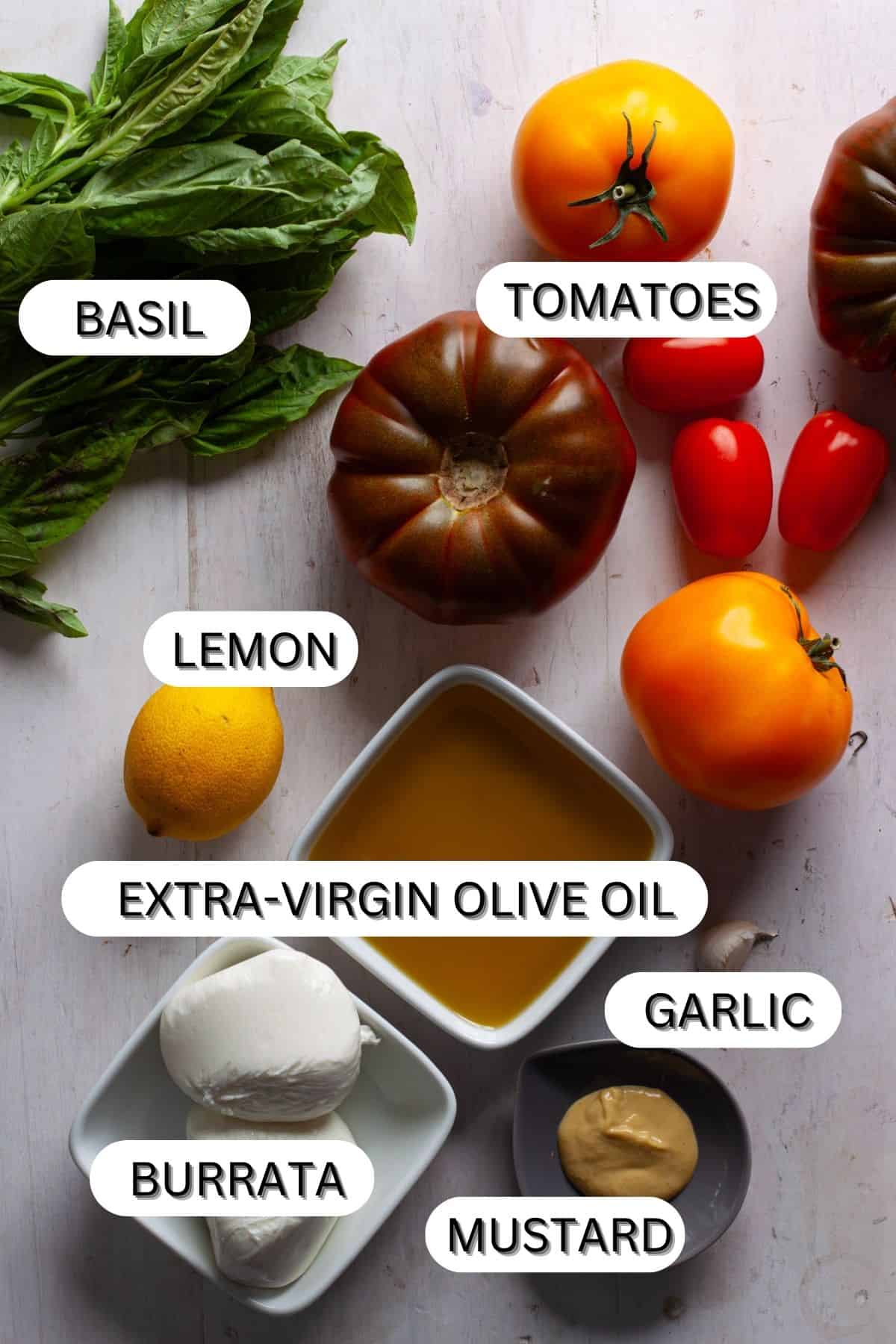 Ingredients for a burrata caprese salad with basil vinaigrette on a white table.