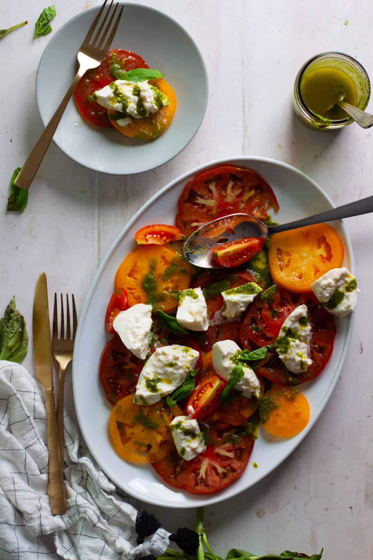Burrata Caprese Salad with Basil Vinaigrette on a serving platter with a small plate of the salad on the side.