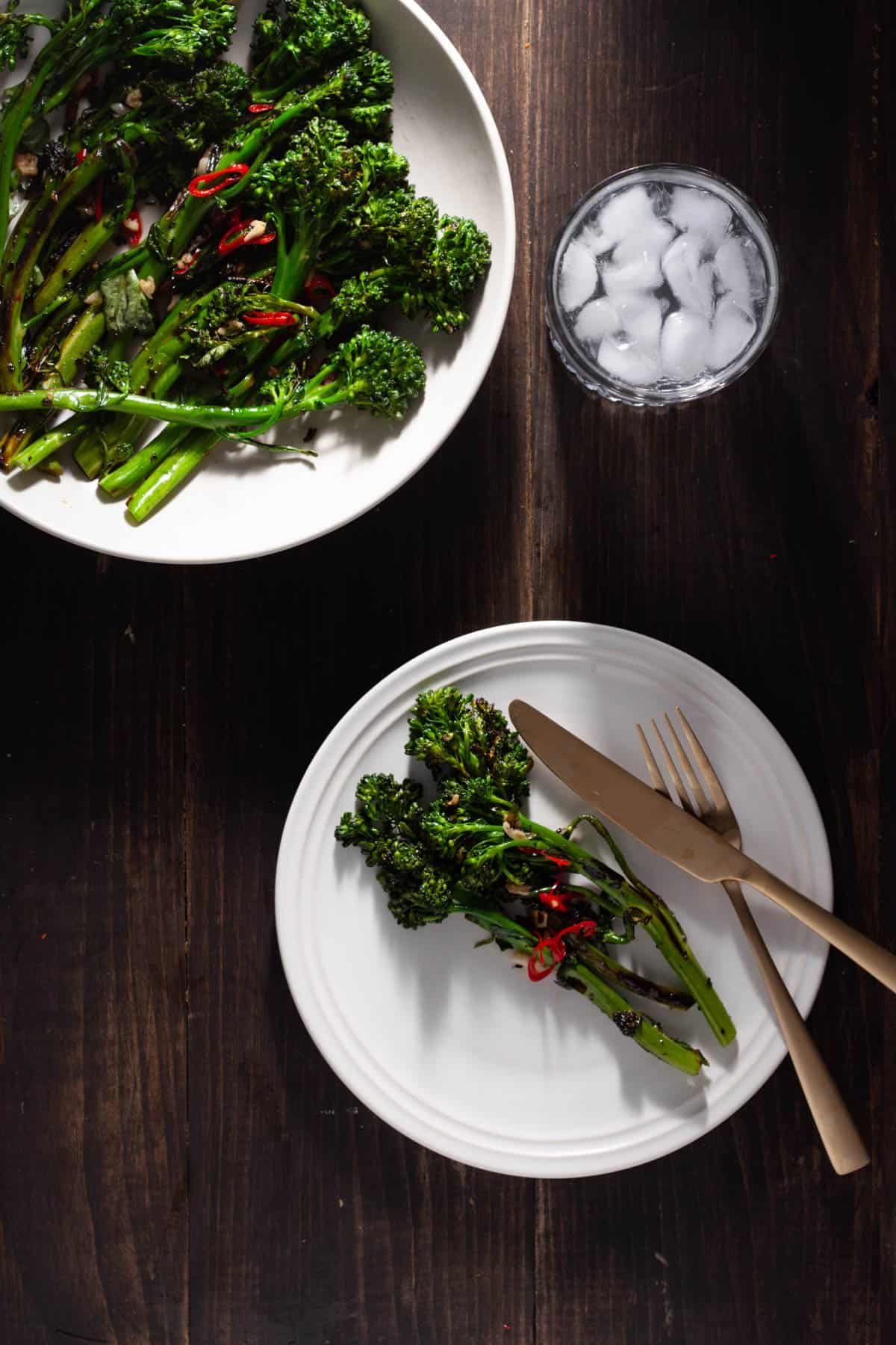Charred broccolini with chili and garlic on a small plate with a bigger serving off to the side.