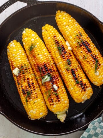Skillet charred corn on the cob topped with butter and dill.