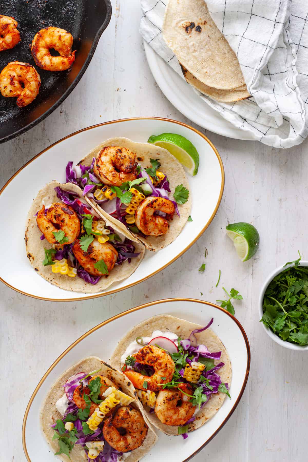 Chili lime shrimp tacos on a couple plates with a skillet of shrimp to the side.