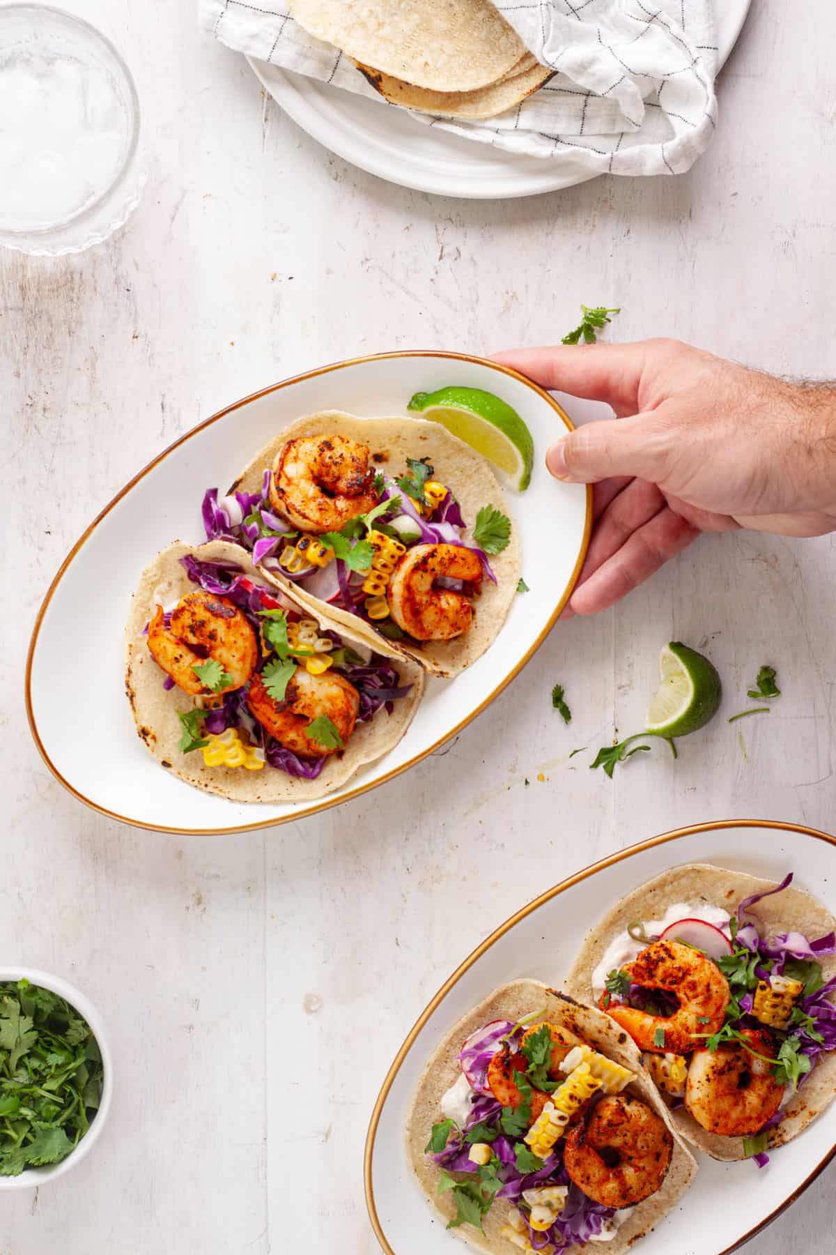 A hand placing a plate of chili lime shrimp tacos.
