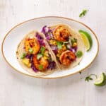 Chili lime shrimp tacos on a small white plate with a lime wedge to the side.
