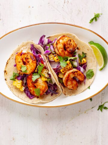 Chili lime shrimp tacos on a small white plate with a lime wedge to the side.