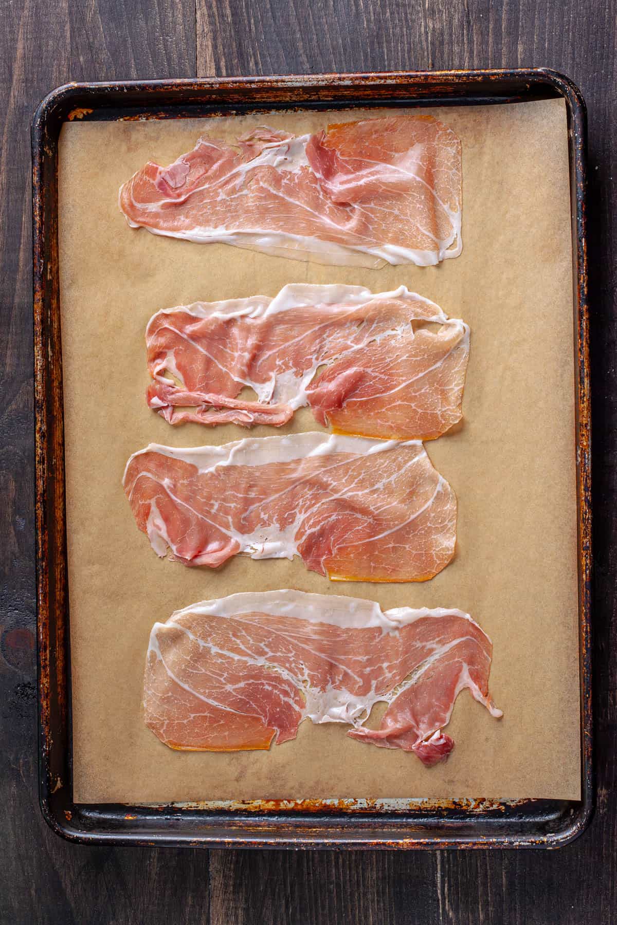 Thin slices of prosciutto on a parchment-lined baking sheet.