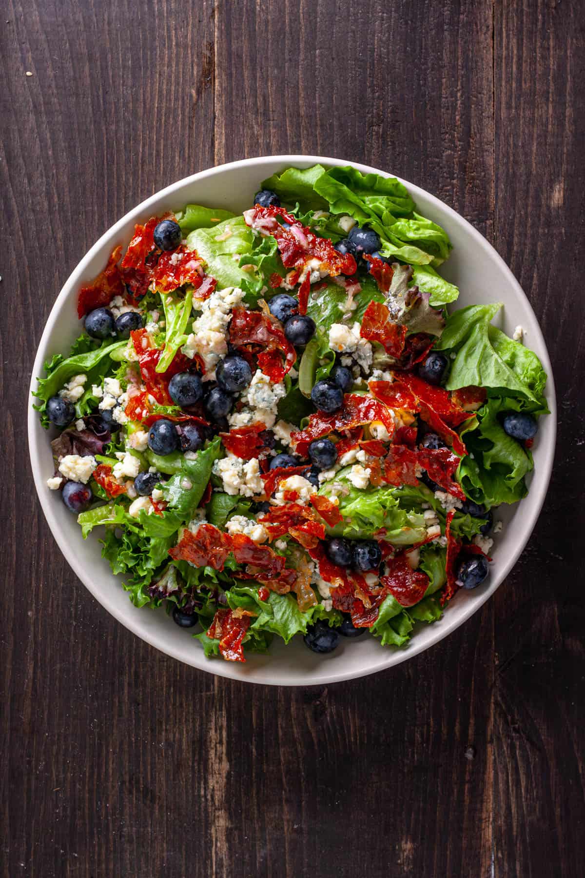 Crispy prosciutto, blueberry and blue cheese salad in a white serving bowl.