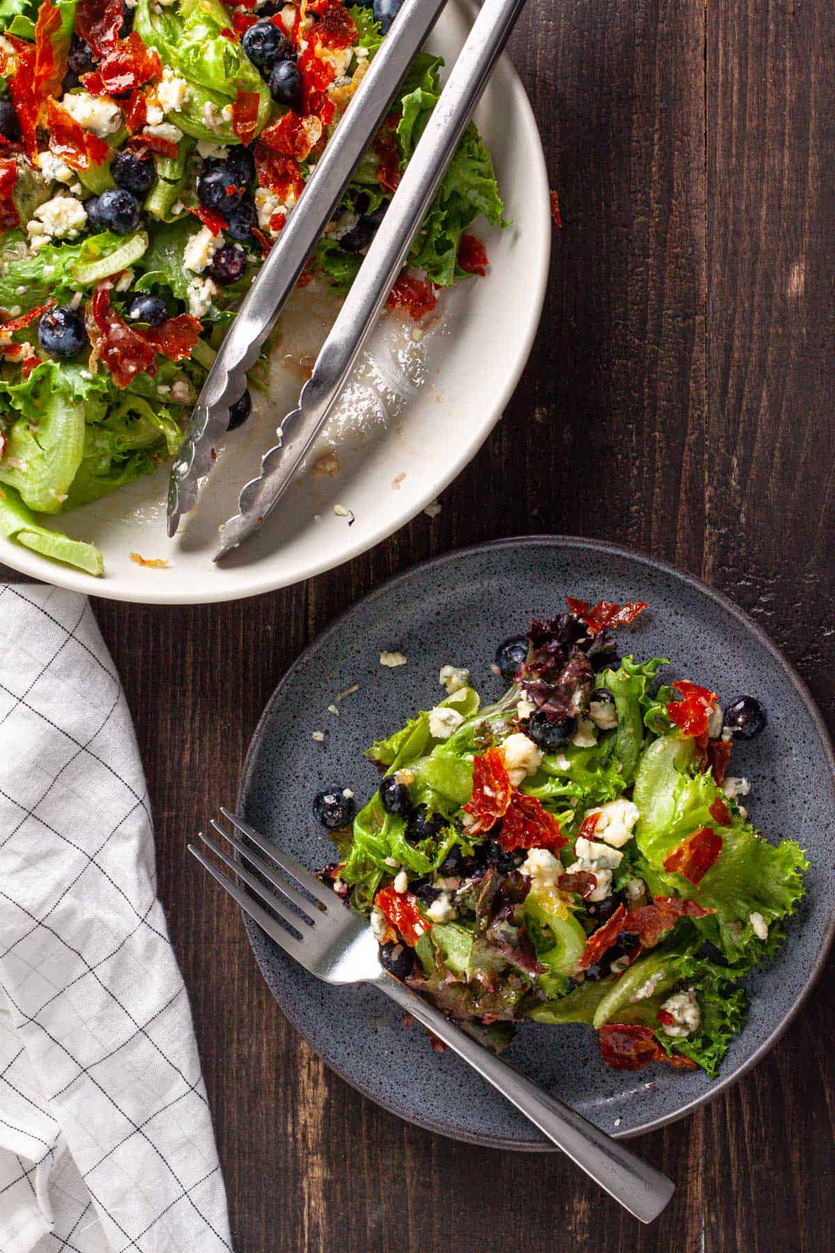 A mixing bowl of crispy prosciutto, blueberry and blue cheese salad with a small serving on a  gray plate.