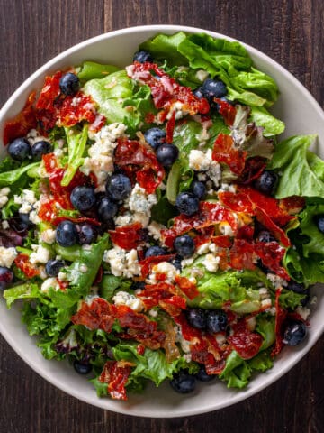 Crispy prosciutto, blueberry and blue cheese salad in a white serving bowl.