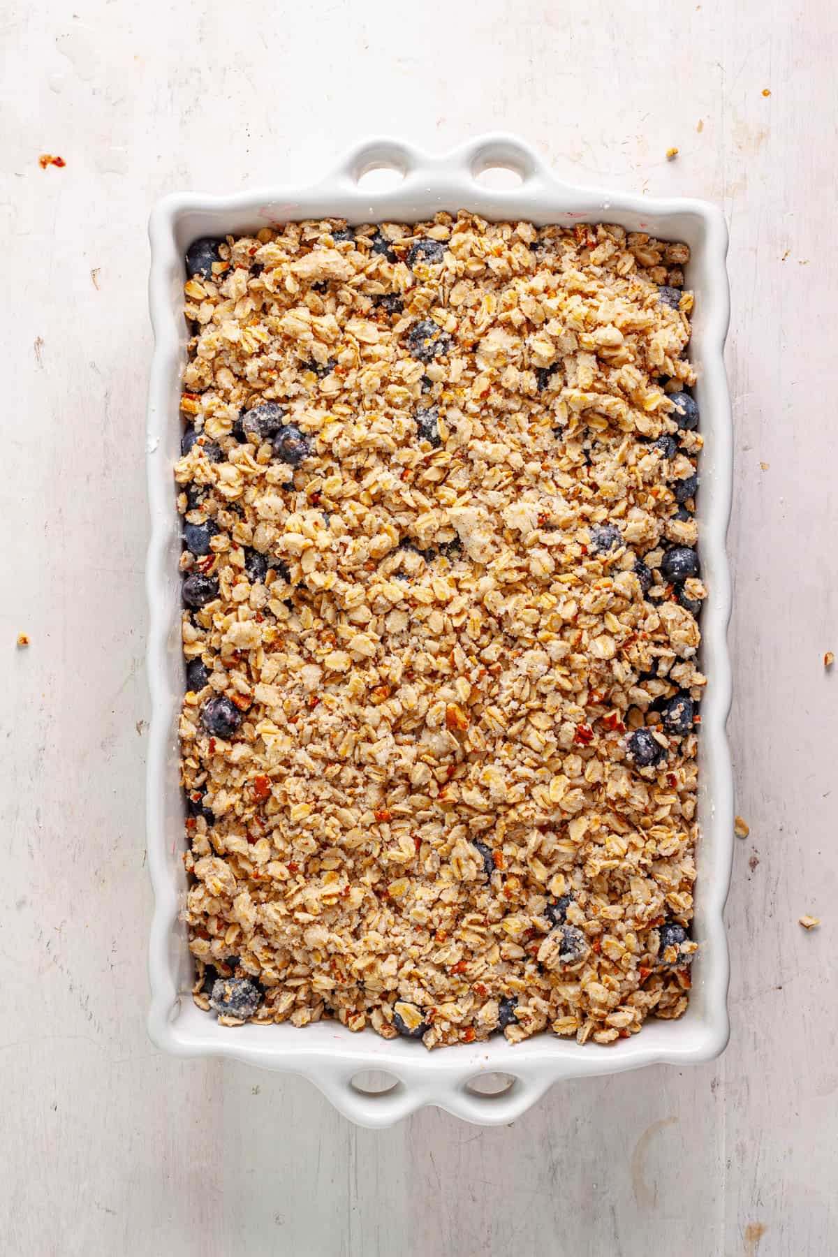 A vegan blueberry crisp unbaked in a white baking dish.
