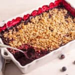 Vegan blueberry crisp in a white baking dish with a scoop taken out.