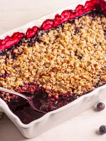 Vegan blueberry crisp in a white baking dish with a scoop taken out.