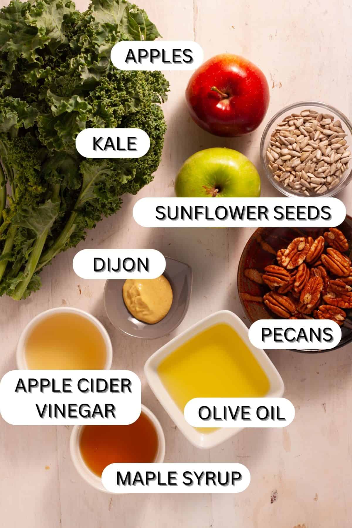 Ingredients for a kale and apple slaw in small bowls on a white table.