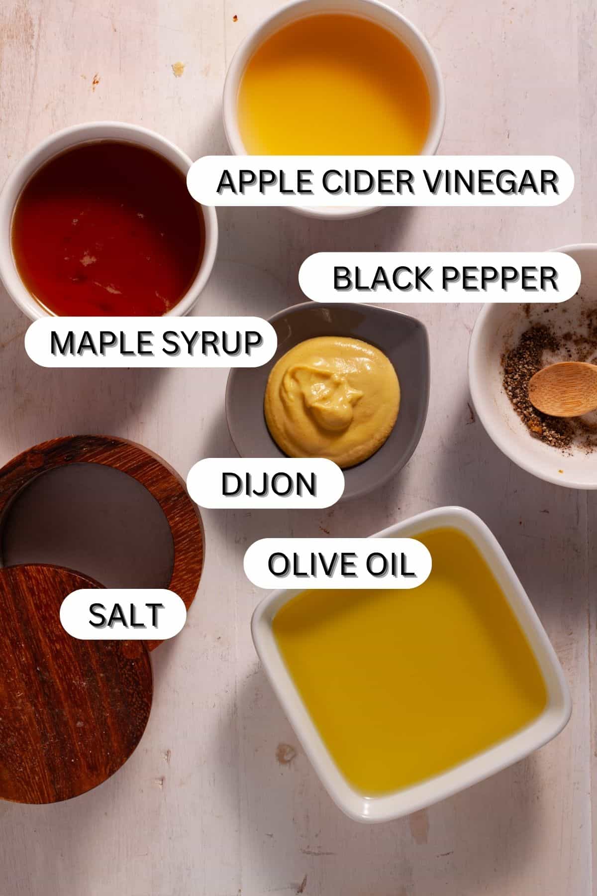 Ingredients for maple dijon dressing in small bowls on white table.