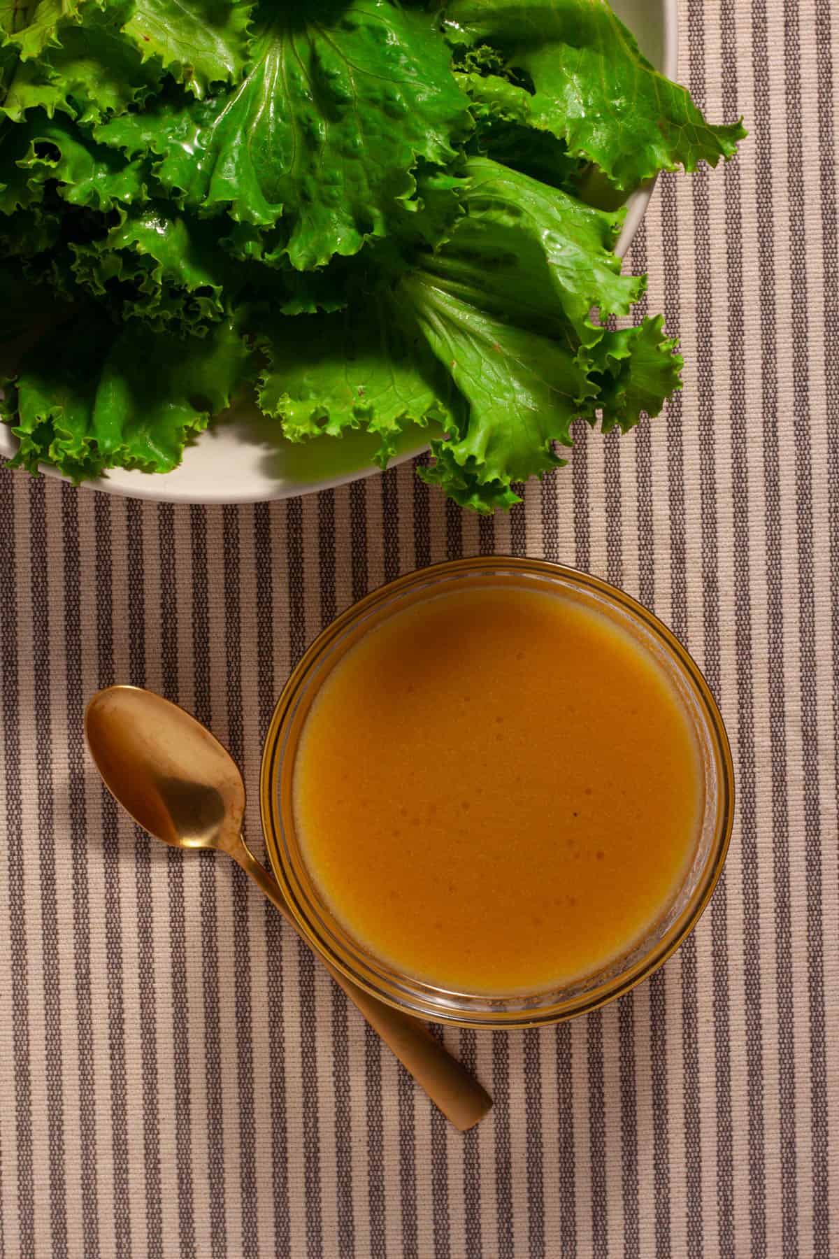 Maple Dijon Dressing in a small bowl on the side of a bowl of greens.