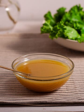Maple Dijon Dressing in a small bowl on a table with a salad and flowers in the background.