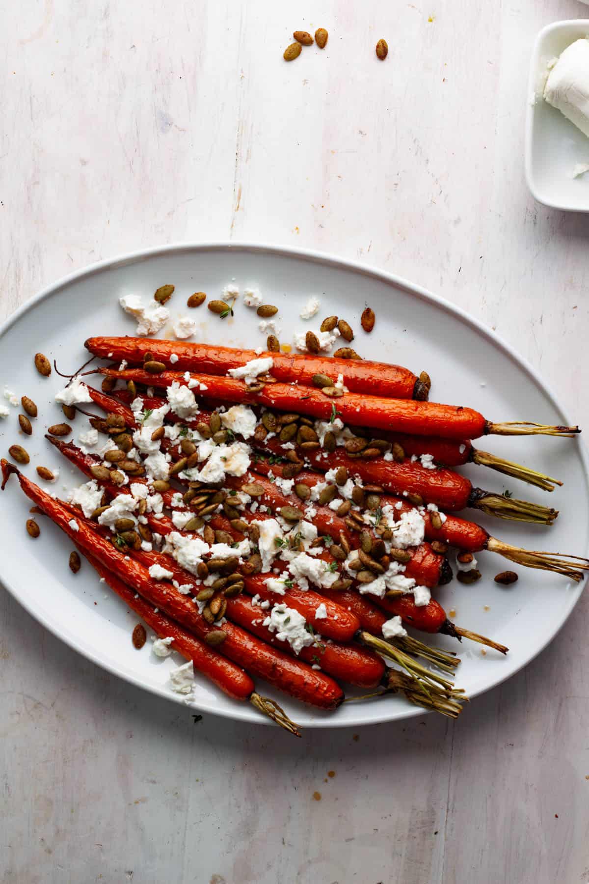 Maple roasted carrots on a white platter topped with crumbled goat cheese and spiced pepitas.